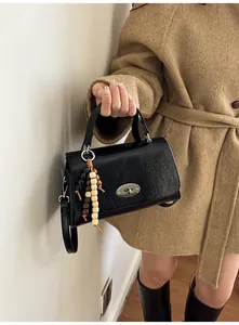 Nahaufnahme der schwarzen Handtasche mit silbernem Drehverschluss und dekorativem Holzperlenanhänger
