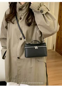 Detail of black lychee grain leather handbag with silver zipper on a beige trench coat
