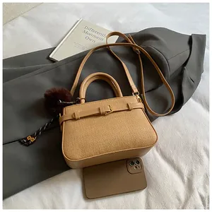 Top view of woven bucket bag with belt buckle detail and plush charm next to a phone