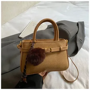 Close-up of light brown woven bucket bag with metal buckle and plush ball charm detail