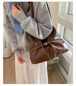 Detail of a pleated brown tote bag featuring soft matte leather and metal buckle decor