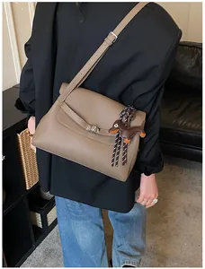 Detail of taupe leather briefcase bag with a cute dachshund charm on a model's outfit
