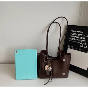 Detail of dark brown tote bag with silver rivets, ice cream charm and blue tablet for scale
