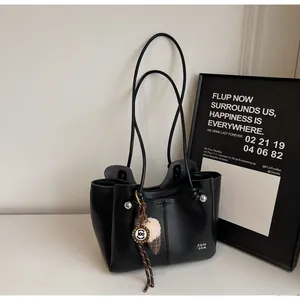 Detail of minimalist black leather tote bag with elegant charms and thin shoulder straps