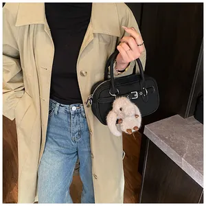 Detail of black Boston handbag with plush sheep charm worn with a stylish trench coat