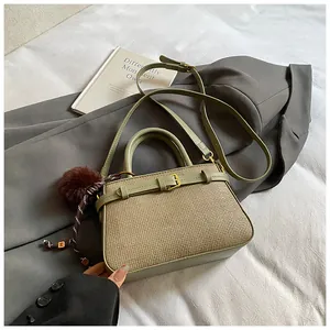 Detail view of green leather and khaki woven bucket bag with pom-pom charm on bed