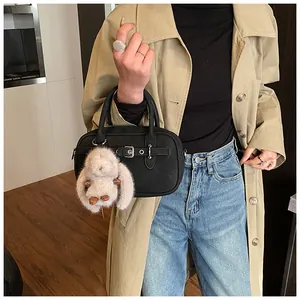 Detail of black leather handbag with a plush rabbit charm shown on a stylish trench coat