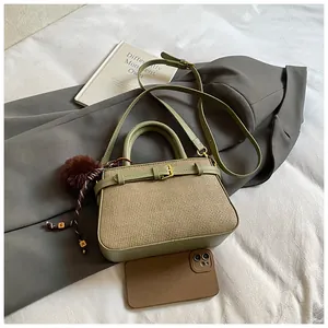 Detail of woven texture bucket bag with metal buckle and soft brown pompom charm