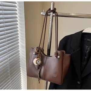 Detail of dark brown tote bag featuring knotted handle and creative ice cream pendant charm