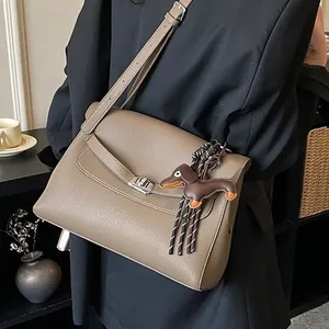 Retro khaki brown leather handbag with dachshund charm shown on shoulder with black blazer