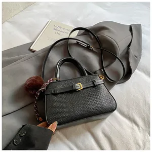 Detail of black woven texture bucket bag with gold buckle and fuzzy brown pompom charm