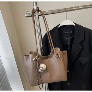 Detail of a brown leather tote bag with stylish plush pom-pom and circular pendant decor