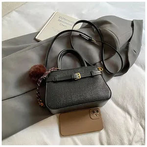 Detail of black woven bucket bag with gold clasp, fuzzy charm and long shoulder strap