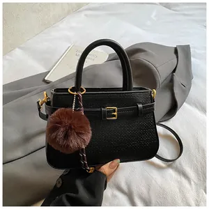 Close-up of black textured bucket bag with gold buckle and plush pompom accessory