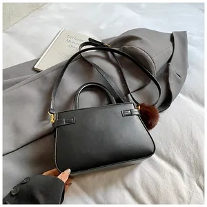 Top view of black trapezoid bucket bag with brown pompom charm on grey blazer