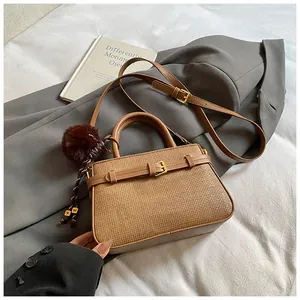 Detailed shot of brown woven bucket bag featuring gold buckle and plush pom-pom charm