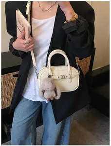 Detail of cream crossbody bag with silver buckle and plush rabbit charm on a model