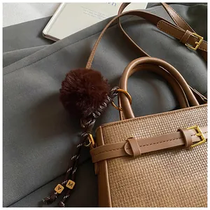 Close-up of brown bucket bag with woven texture, plush ball charm and gold hardware