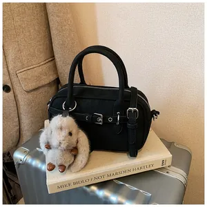 Detailed view of a black Boston handbag with plush bunny charm on a vintage suitcase