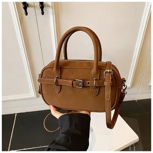 Detail of a brown leather crossbody bag with retro buckle and textured finish