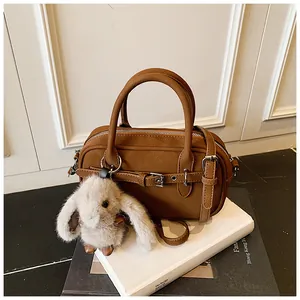 Detailed view of a brown faux leather Boston bag with plush bunny charm on white props