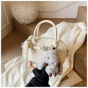 Detailed view of a cream Boston handbag with plush rabbit charm and silver metal buckles