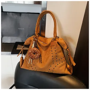 Details einer braunen Wildleder-Tote Bag mit Nieten und Plüsch-Anhänger auf Ledersitz