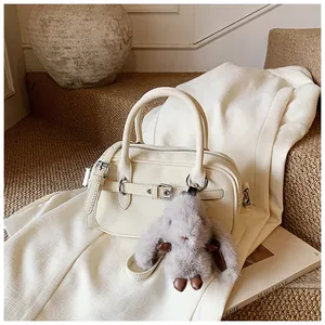 Detail view of cream leather boston bag featuring a plush bunny charm and shoulder strap