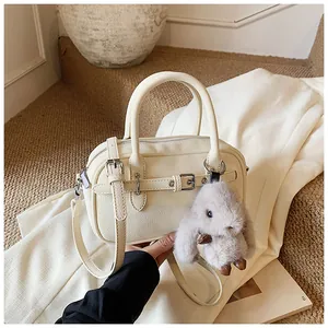 Close-up of beige lychee grain leather boston bag with detachable strap and plush rabbit charm
