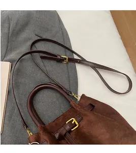Detalle de bolso bucket de ante marrón con hebillas doradas sobre una chaqueta