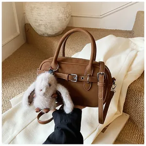 Close-up of brown leather handbag with a white plush bunny charm on white clothing