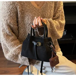 Detail einer schwarzen Wildleder-Handtasche mit goldener Schnalle und rundem Griff im Alltag