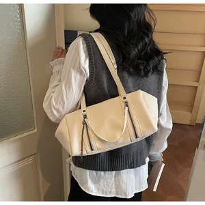 Detail of off-white leather shoulder bag with decorative zippers and metal chain charm