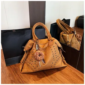 Detail der braunen Wildledertasche mit Nieten und Plüsch-Donut-Anhänger auf Holz