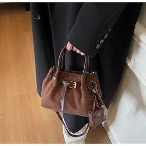 Detail der Wildleder-Eimertasche mit Lederriemen und dekorativem kariertem Schal