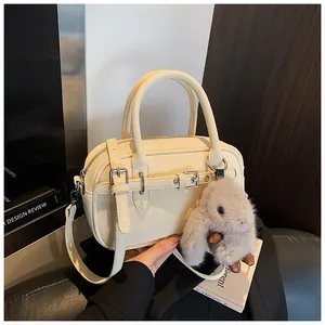 Detail of beige faux leather handbag with buckled strap, plush charm, and dual handles