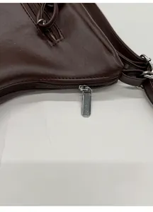 Close-up of a silver rectangular zipper on a matte dark brown leather tote bag