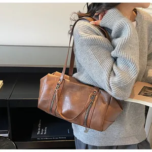 Brown vintage faux leather underarm bag with zipper details worn by a model in a casual setting