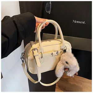 Close-up of beige crossbody bag with plush bunny charm and textured faux leather detail