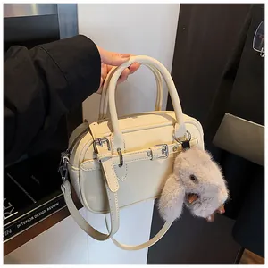 Detail of beige textured leather handbag featuring decorative straps and a plush bunny charm