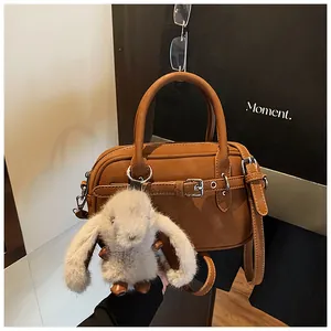 Detailed view of brown leather bag texture featuring a cute plush bunny charm and silver buckle