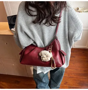 Detail of vintage burgundy shoulder bag with side pockets and plush dog charm accessory