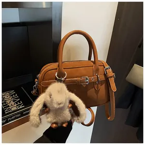 Detail view of caramel brown crossbody bag with litchi grain and grey plush rabbit charm