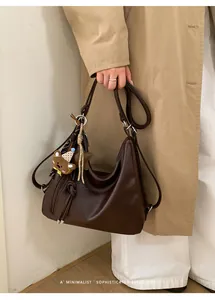 Detail of vintage brown leather tote bag featuring a cute bear pendant on a model