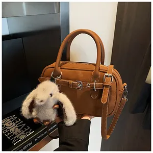 Close-up of brown textured leather Boston bag featuring a white bunny plush pendant