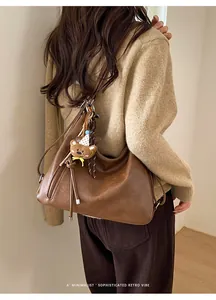 Detailed close-up of brown vintage leather tote bag with cute bear charm and shoulder strap