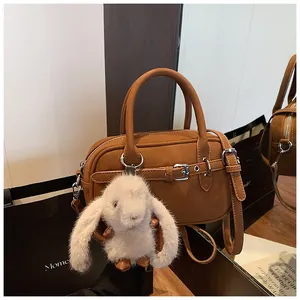 Brown leather crossbody bag detail featuring a cute white bunny plush keychain on the handle