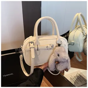 Detail view of cream-colored vintage bowling bag with leather straps and plush rabbit charm