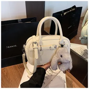 Close-up of beige lychee texture handbag with buckle detail and plush rabbit charm