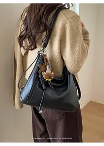 Detail of black leather hobo bag with cute bear pendant and star charm on shoulder strap